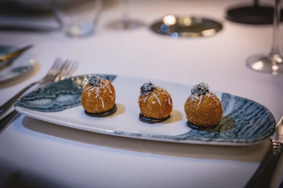 Three golden arancini on a long patterned plate