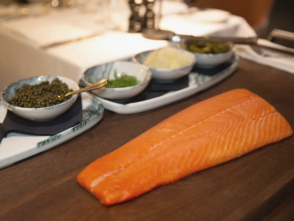A side of house-smoked salmon on a board with pickled garnishes