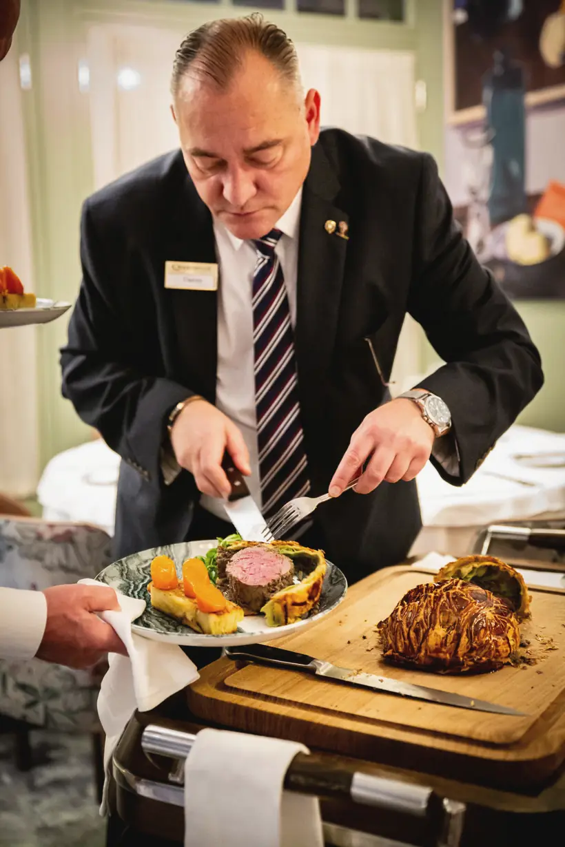 A member of the Sage team carving a Beef Wellington on the trolley beside the table