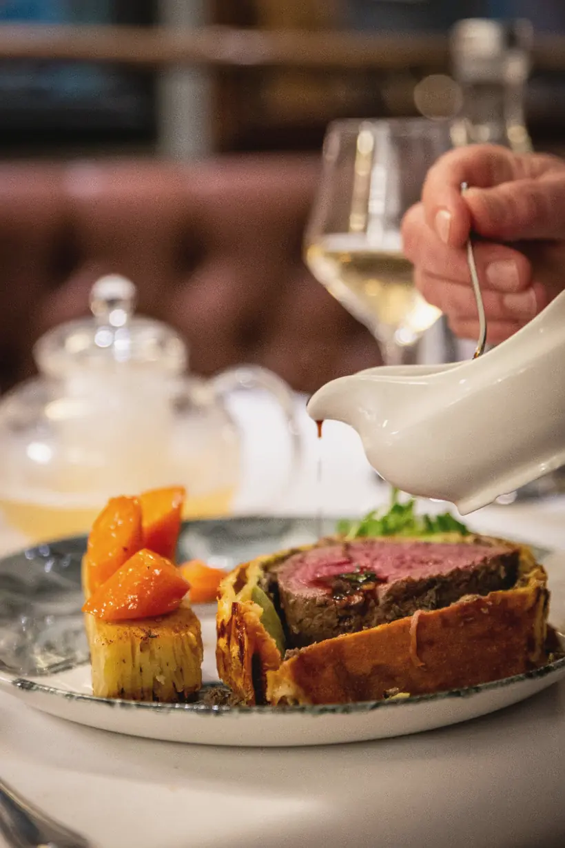 Bordelaise sauce poured from a sauce boat over a plated Beef Wellington